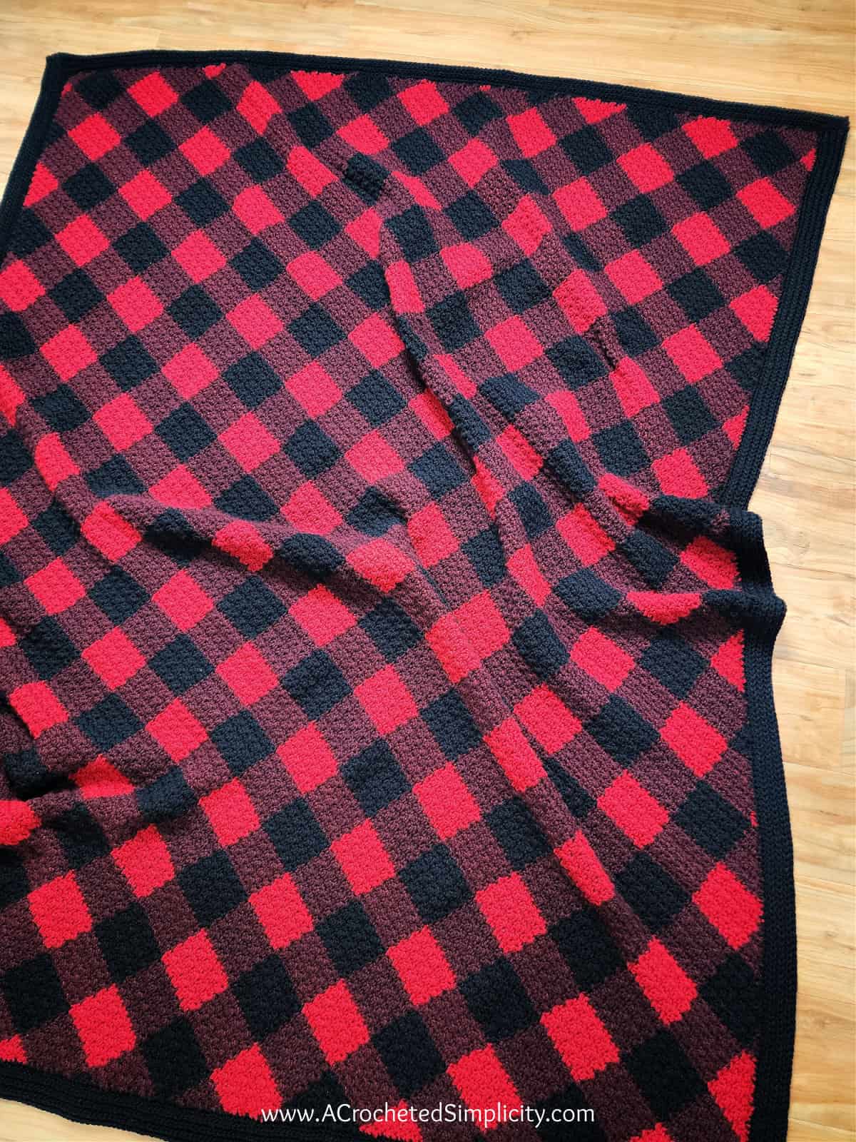 Corner to corner crochet buffalo plaid blanket laying on a wood floor.