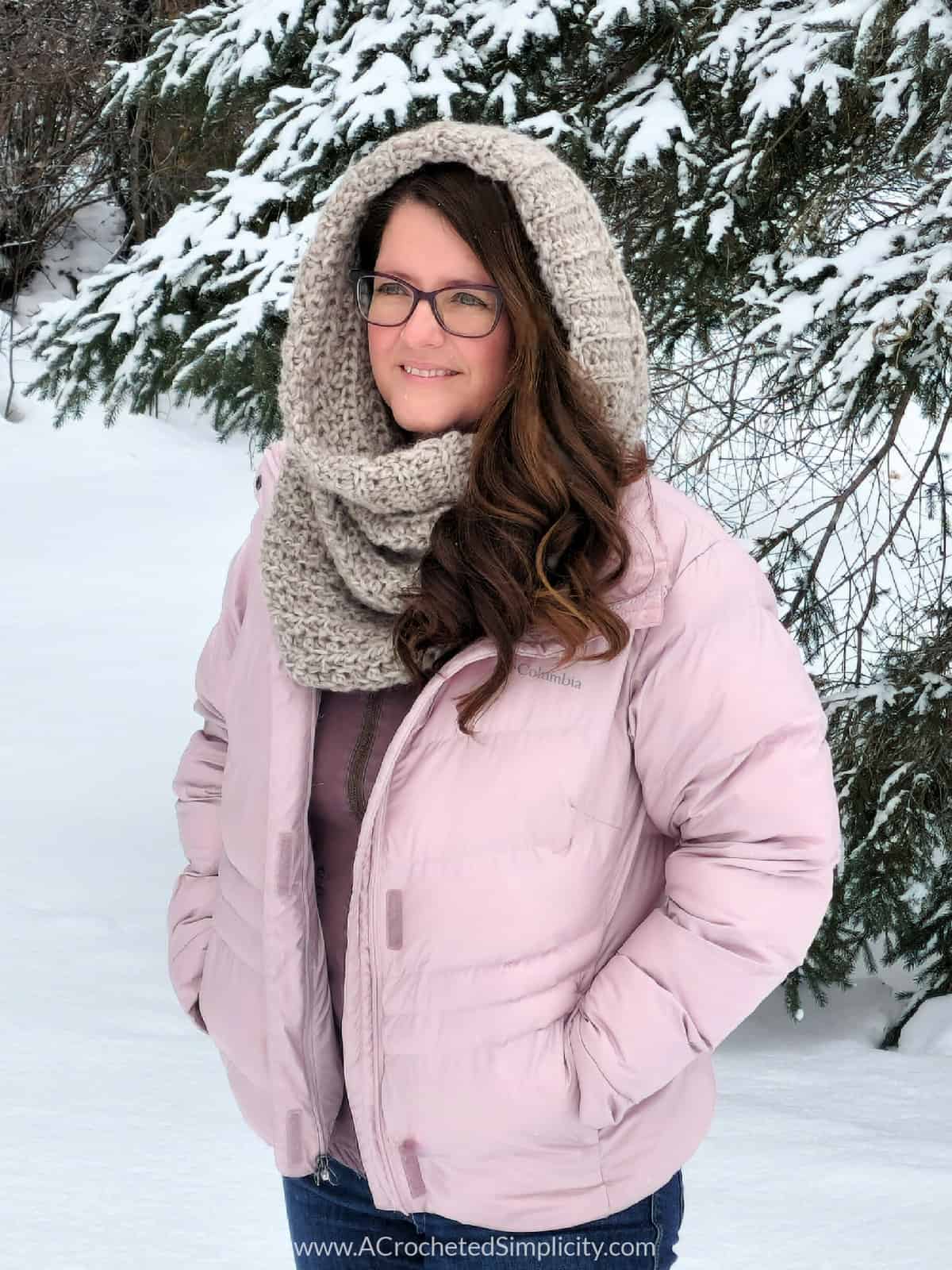 Image of woman in pink jacket outside in winter landscape wearing crochet hooded cowl.