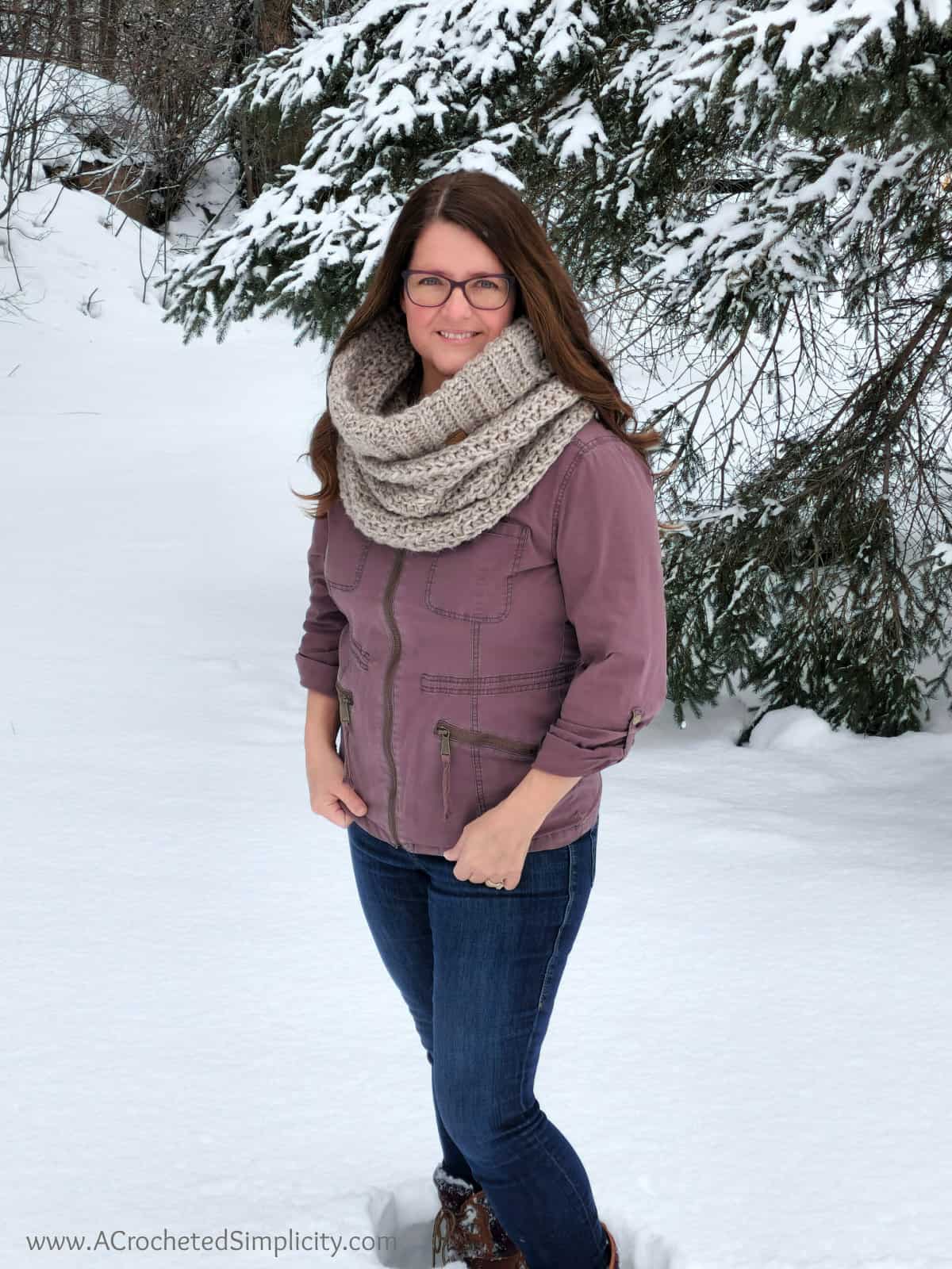 Picture of woman outside in winter in front of pine tree wearing chunky crochet cowl.