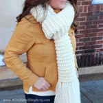 Close up of woman wearing a cream colored knit look crochet scarf.