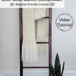 Knit look crochet scarf hanging on a wooden blanket ladder with potted plant.