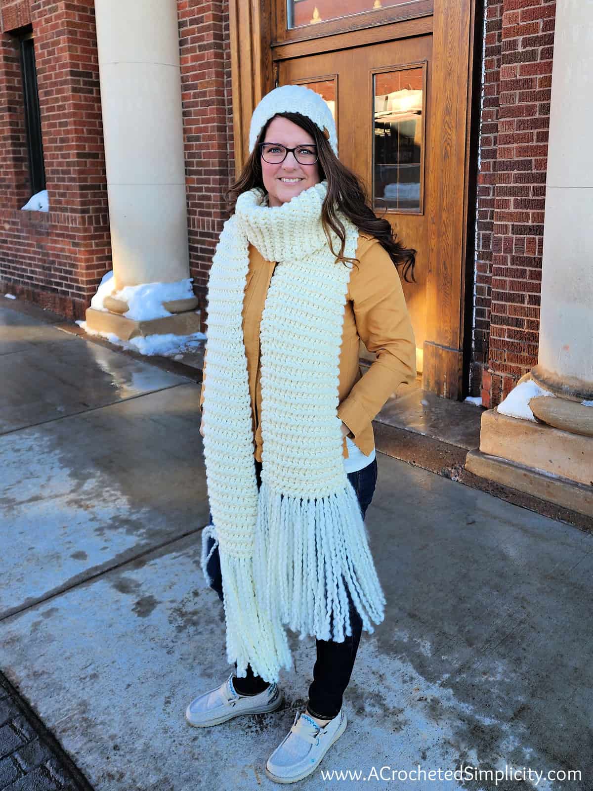 Woman modeling a wide knit look crochet scarf and beanie in cream.