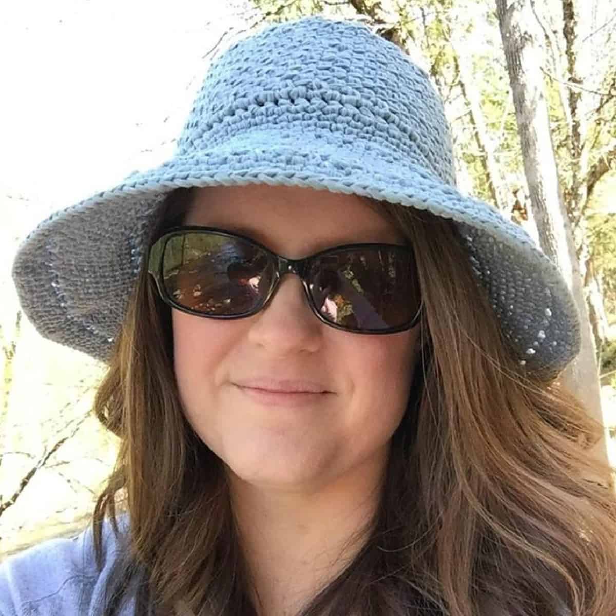 Woman wearing dark sunglasses and wearing a light blue crocheted sun hat.