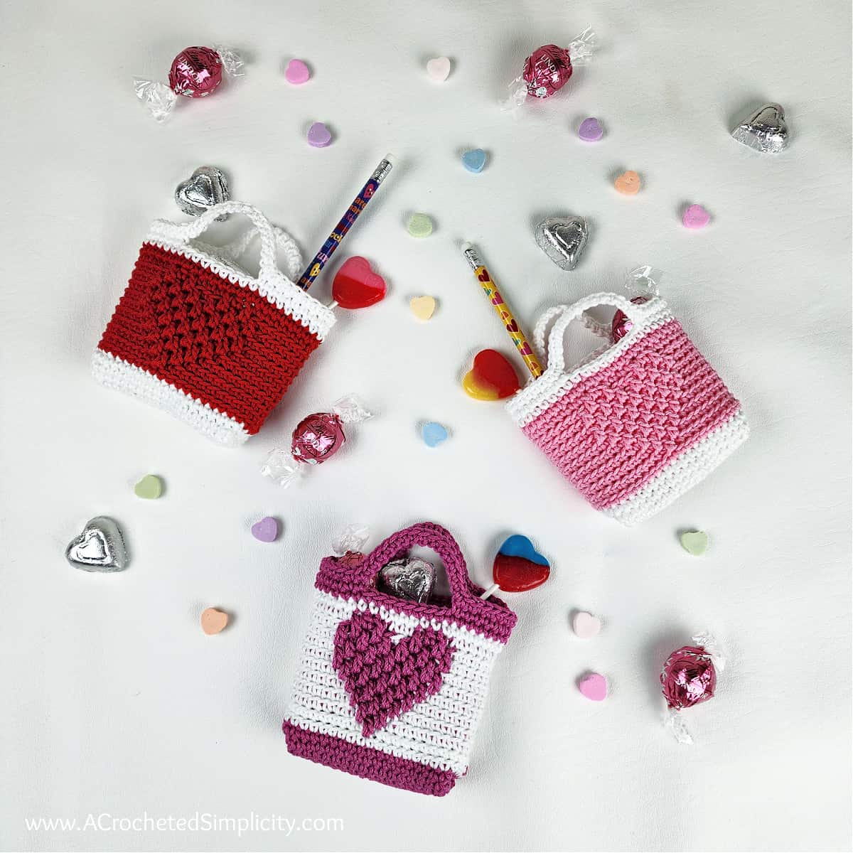 Three small crochet valentine treat bags in red, white and pinks with small candies.