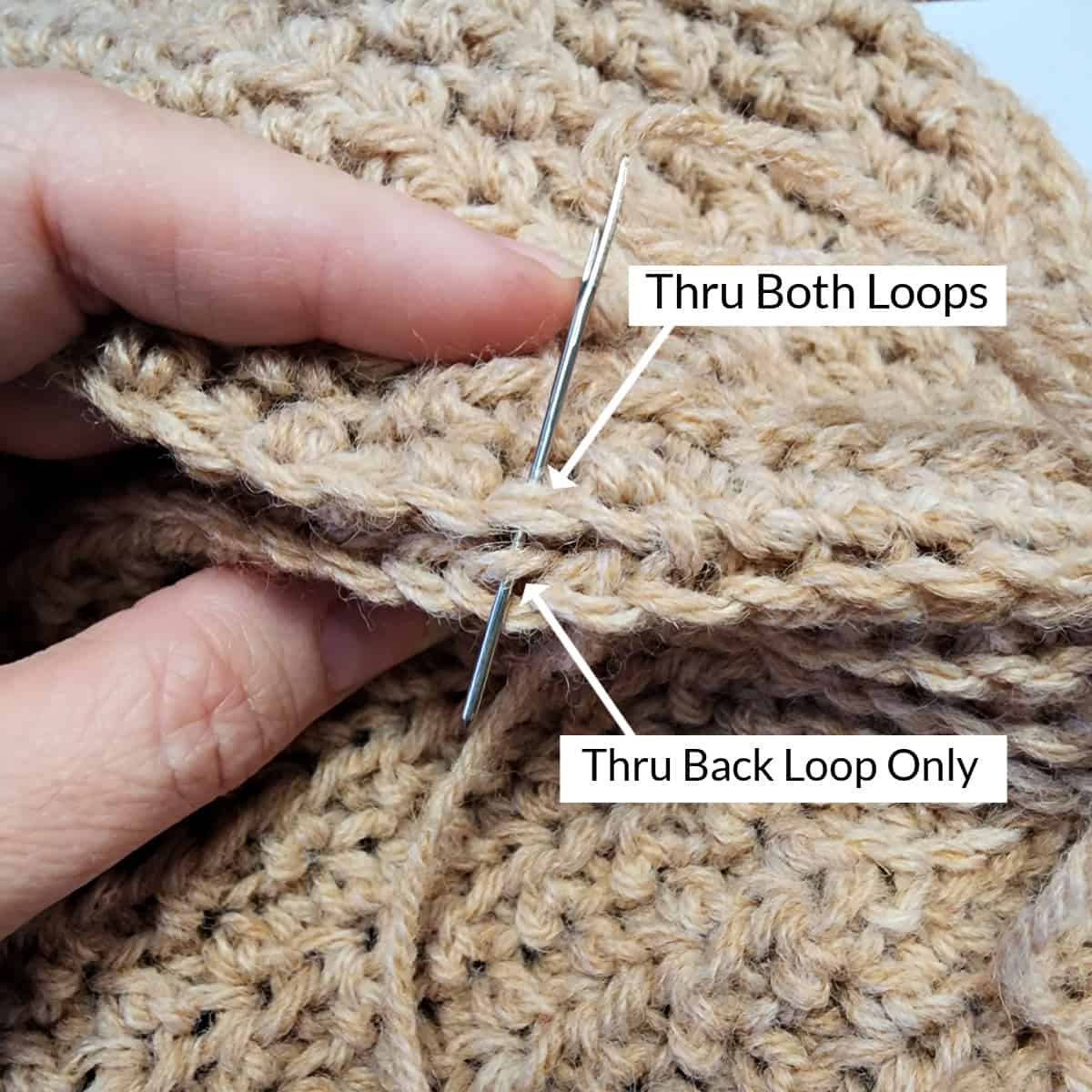 Yarn needle and arrows showing how to seam the middle of the crochet hat seam.