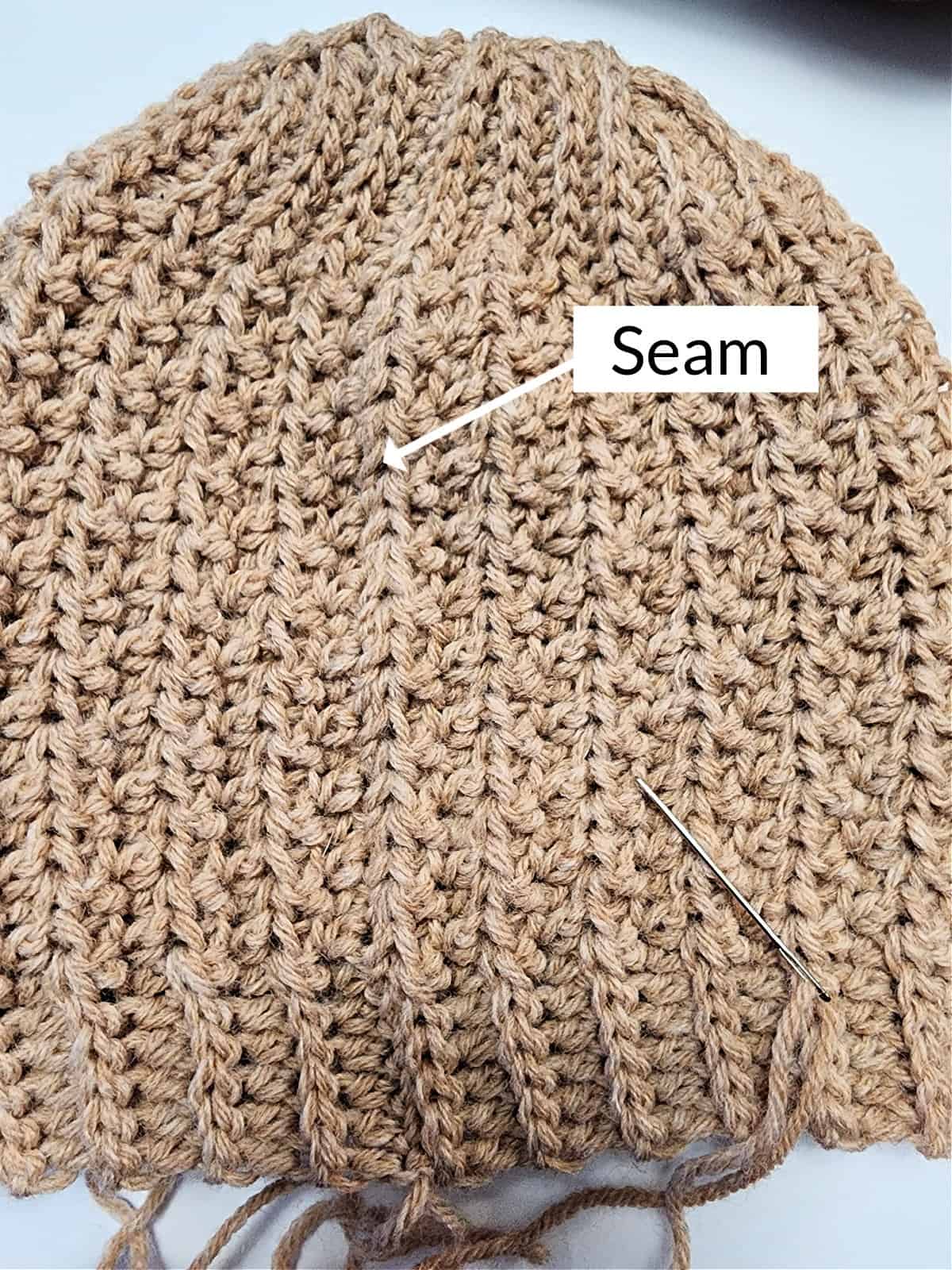 Brown crochet hat laid flat with a arrow pointing at the invisible seam.