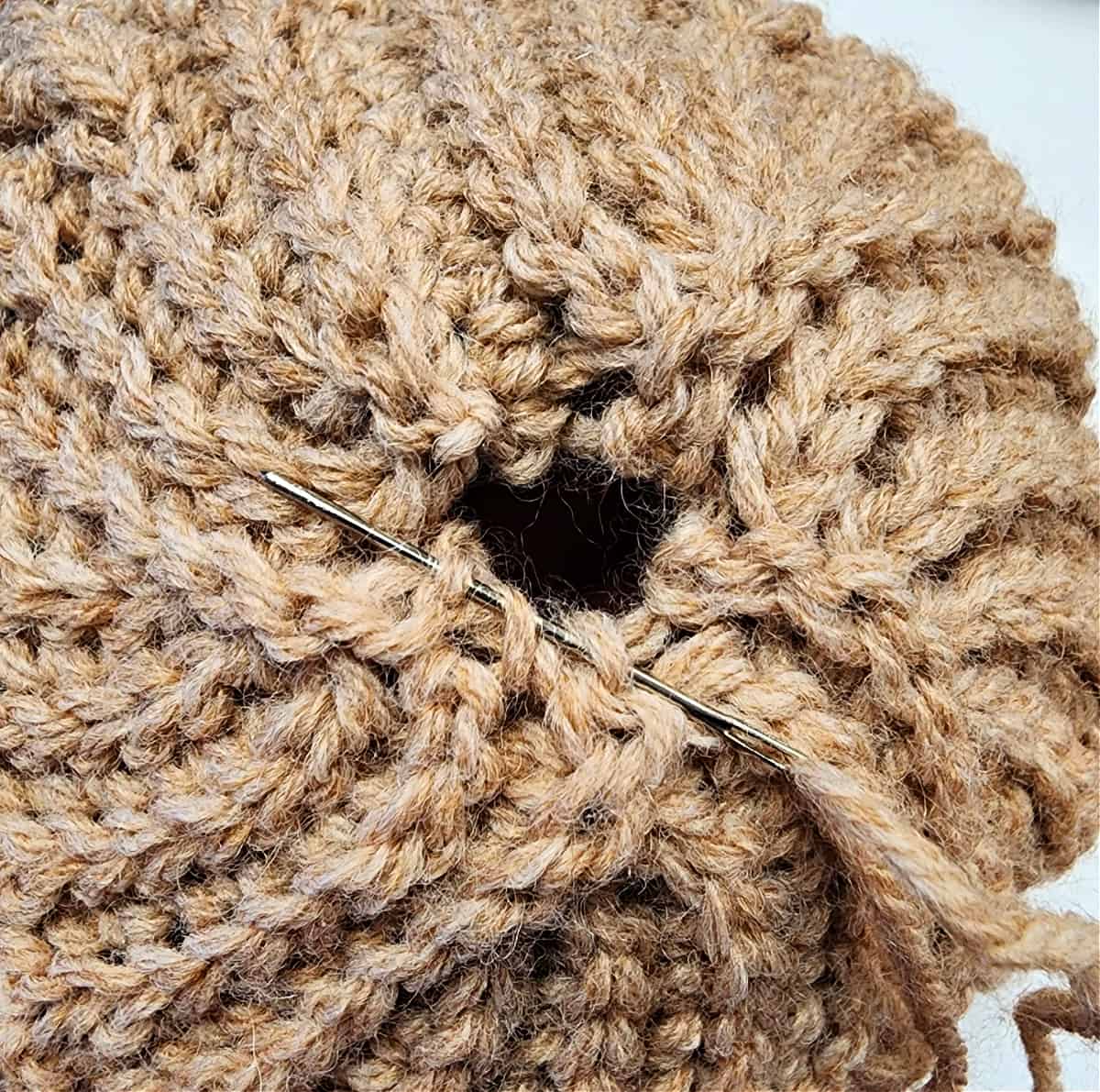 Crochet hat with gap in crown being sewn closed with a yarn needle and tail of yarn.