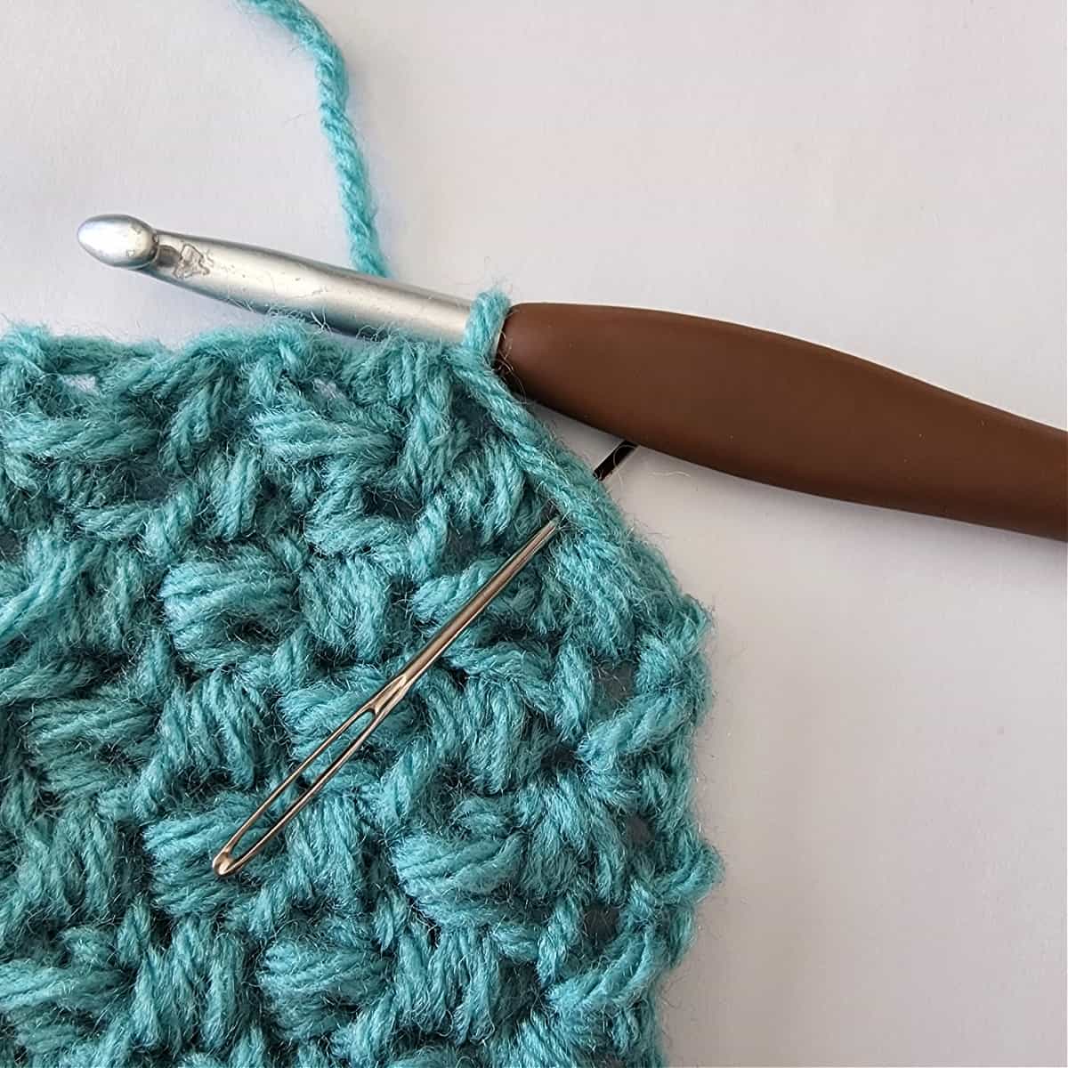 Close up showing how to work the last stitch to complete a mini bean stitch corner to corner square.