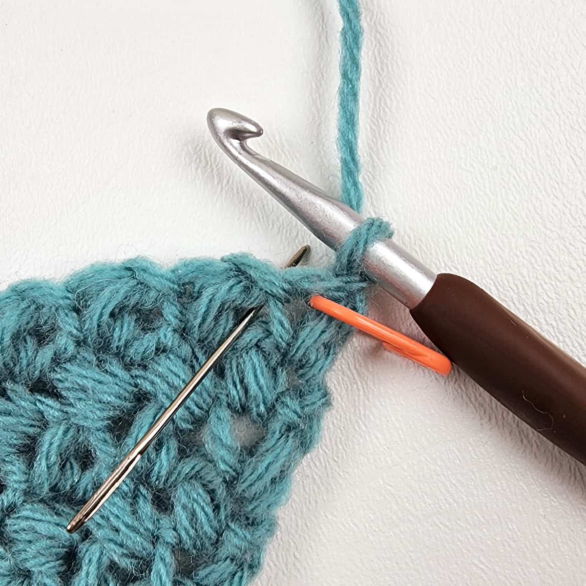 Small swatch of c2c mini bean stitch, brown crochet hook, orange stitch marker and yarn needle.