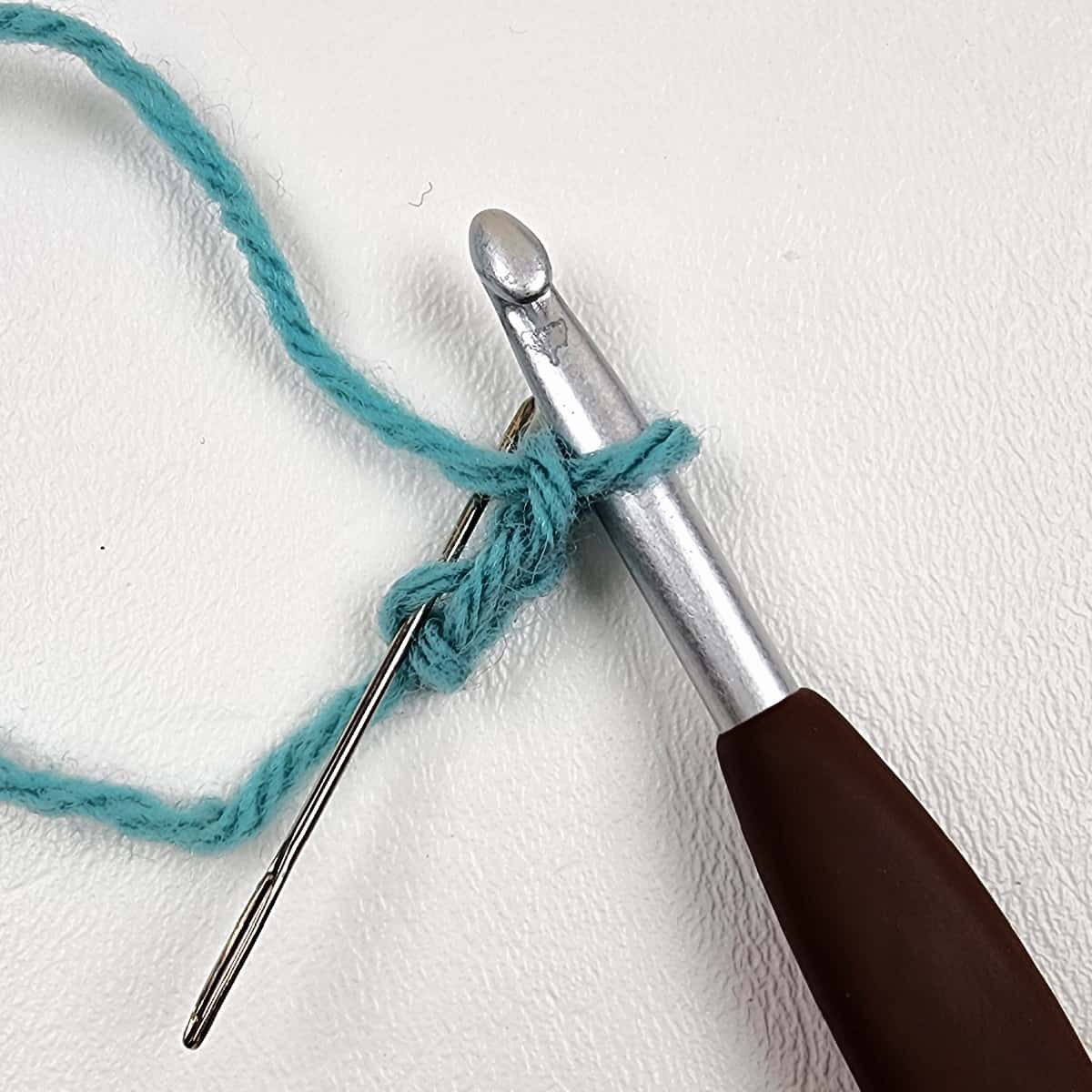 Brown crochet hook and green yarn with a chain two.