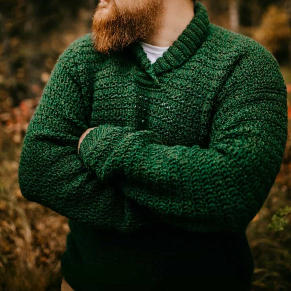 Hunter green shawl collar crochet sweater modeled by a man in the woods.