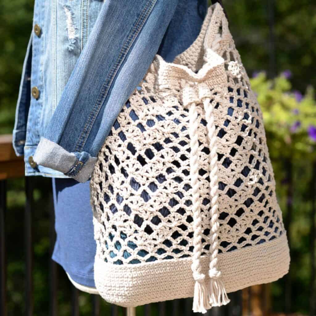 Cream colored crochet bag with a rope tie closure and leather shoulder strap.