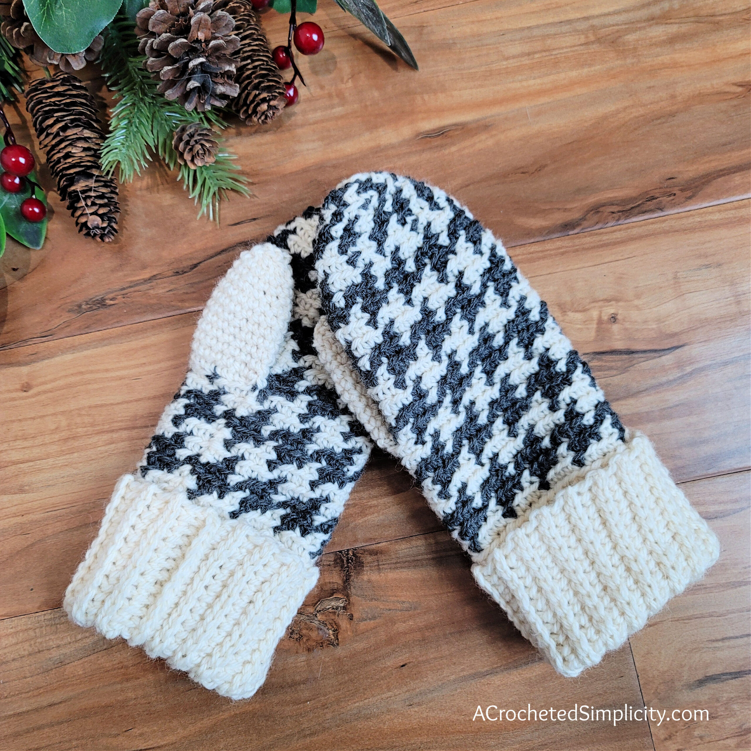 Cream and charcoal grey houndstooth crochet mittens laying on wood floor.