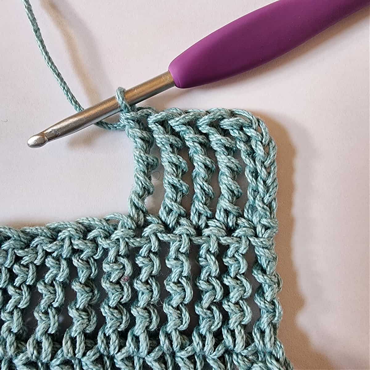 Small blue green crochet swatch showing a chainless triple treble and four triple treble crochet stitches.