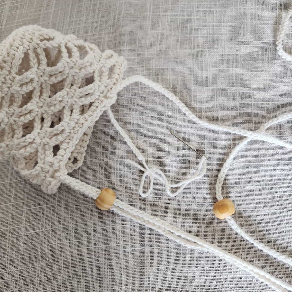 Close up of second hanging strap being attached to crochet hanging plant basket.