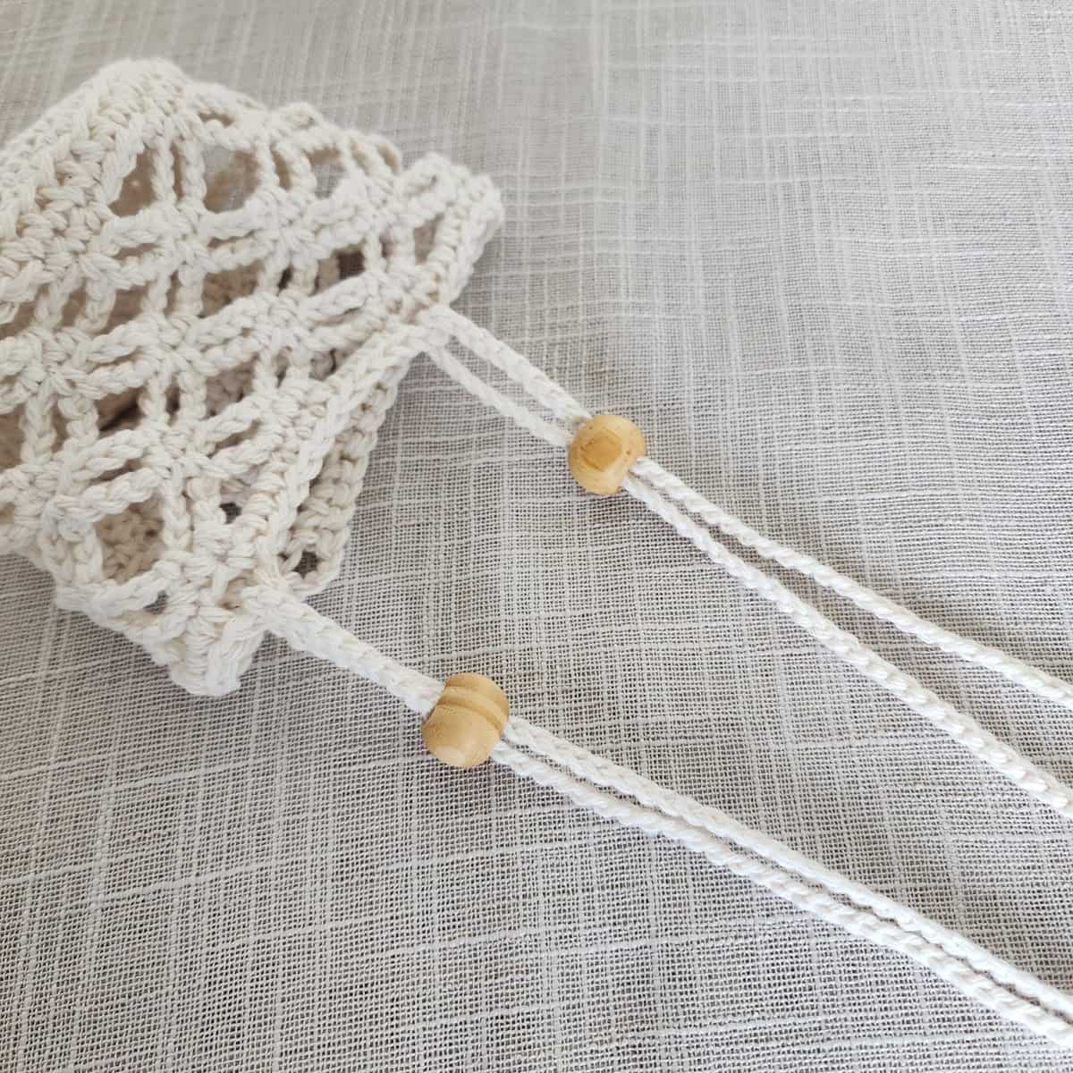 Close up of crochet plant hanger with wooden bead on two hanging straps.