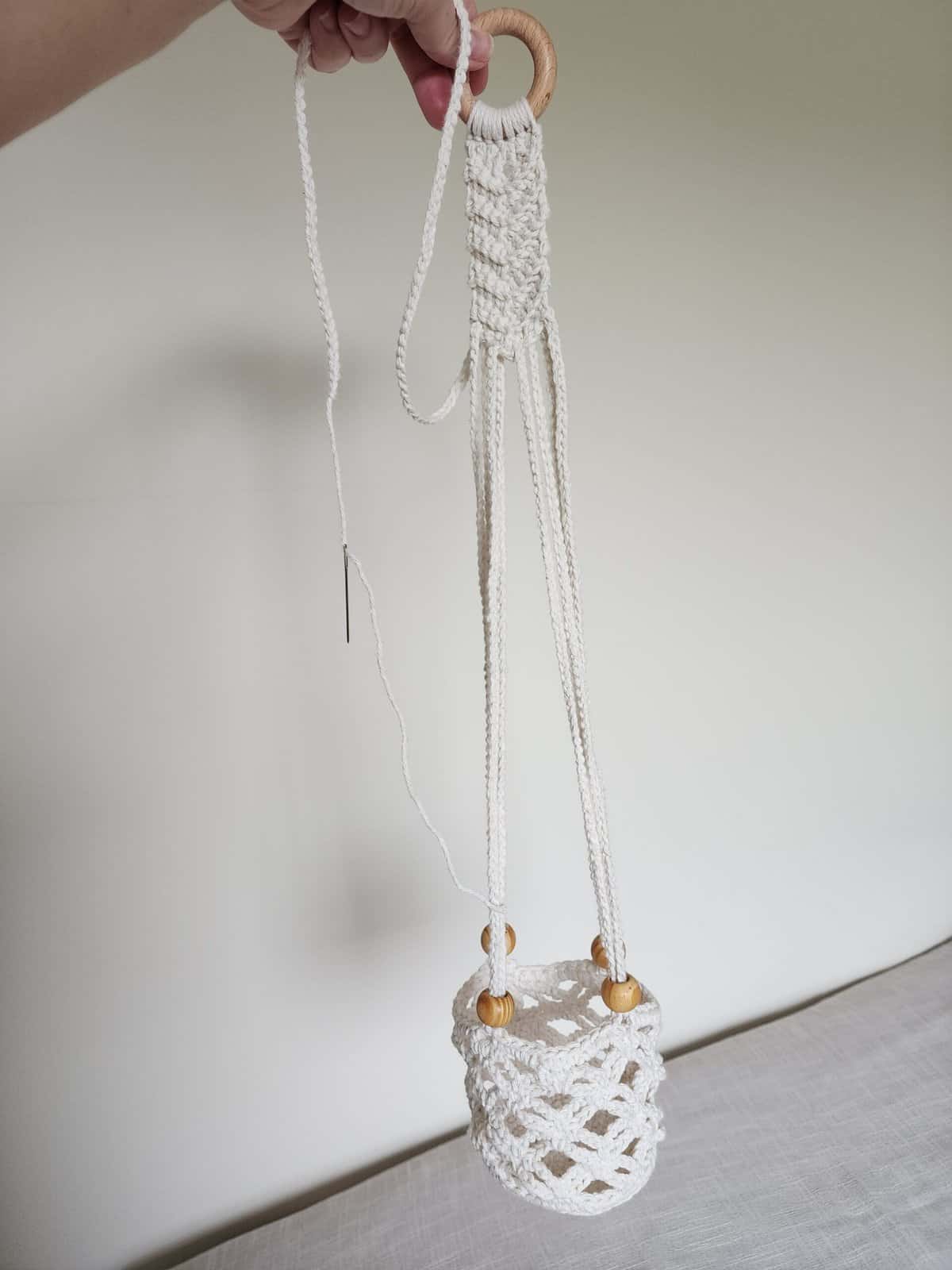 Hand holding crochet plant hanger up to adjust length of straps.