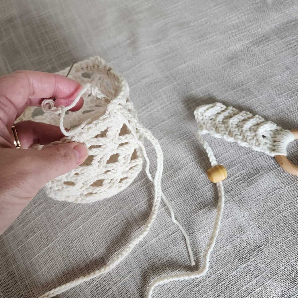 Hand holding crochet plant hanger basket and attaching hanging strap.