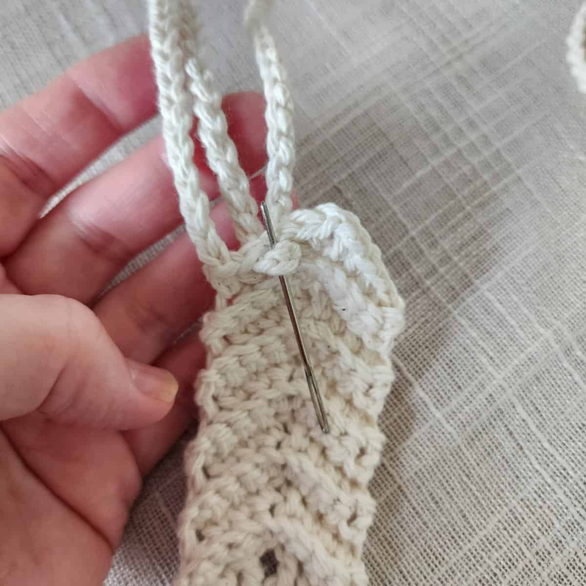 Yarn needle showing how to loop crochet hanging straps to plant hanger.