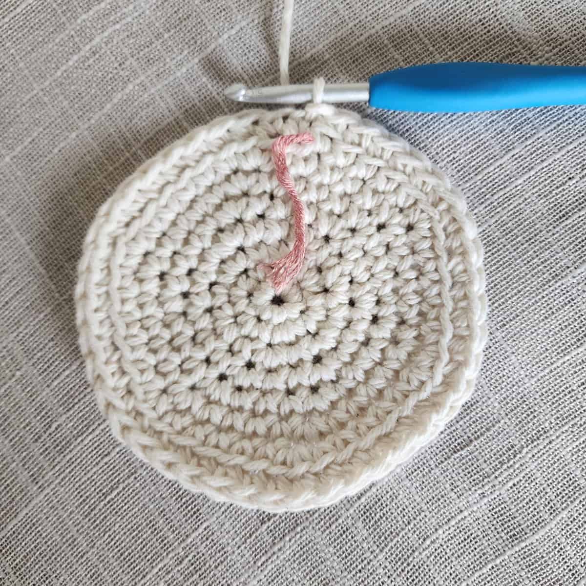 Small ecru crochet circle with blue crochet hook.
