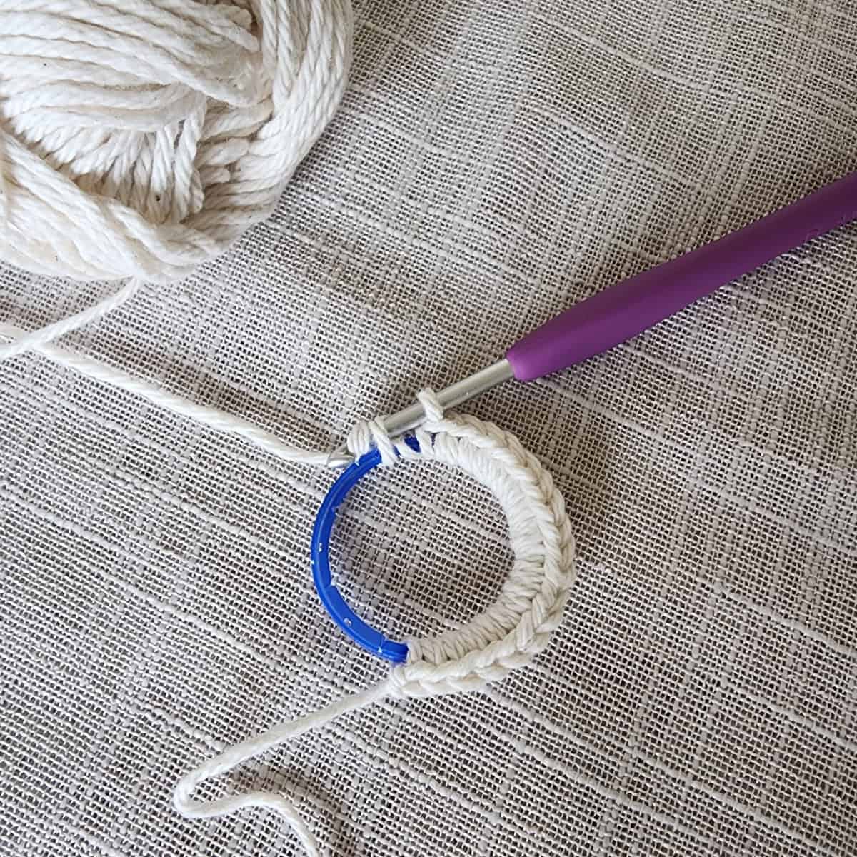 Blue milk jug ring being covered with ecru yarn to create a plant hanger ring.
