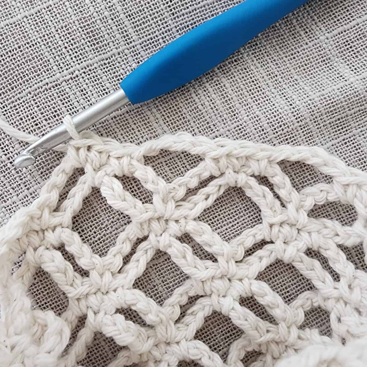 Close up of last round of plant basket being crocheted with blue crochet hook.