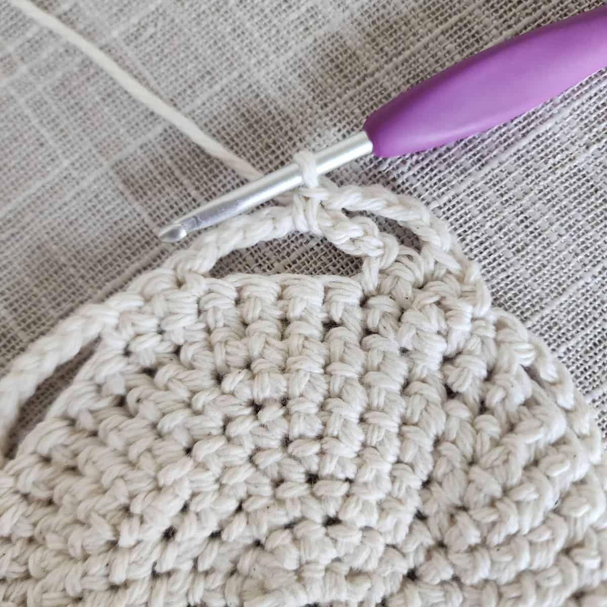 Close up of purple crochet hook making crochet lace on plant basket.