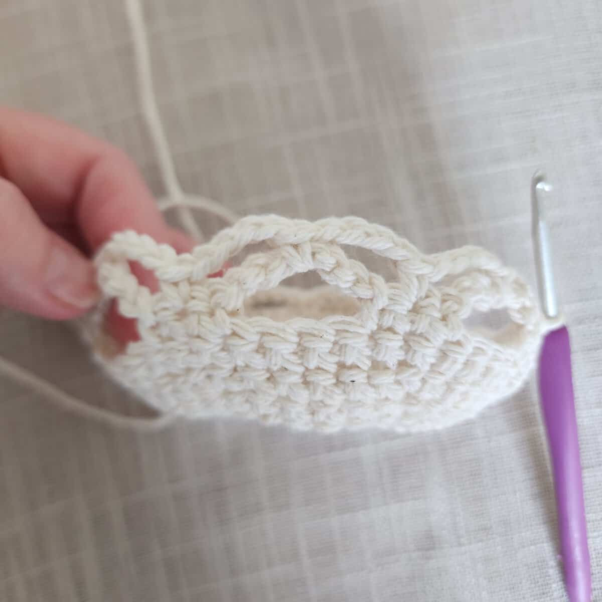 Hand holding beginning of crochet plant hanger basket.