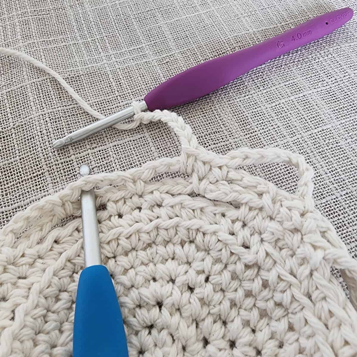 Purple crochet hook crocheting lace and blue crochet hook showing where to work the next stitch.