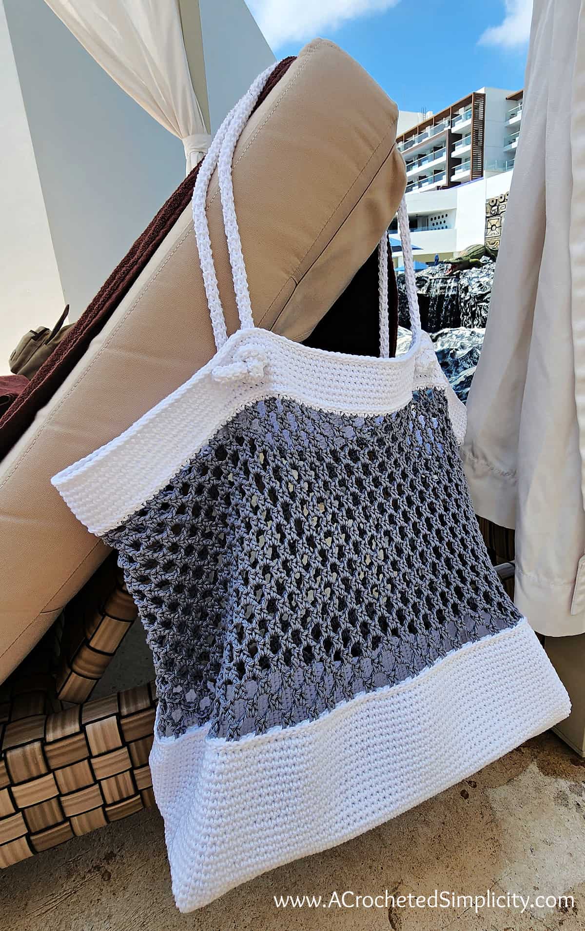 White and grey crochet beach bag hanging on pool lounger.