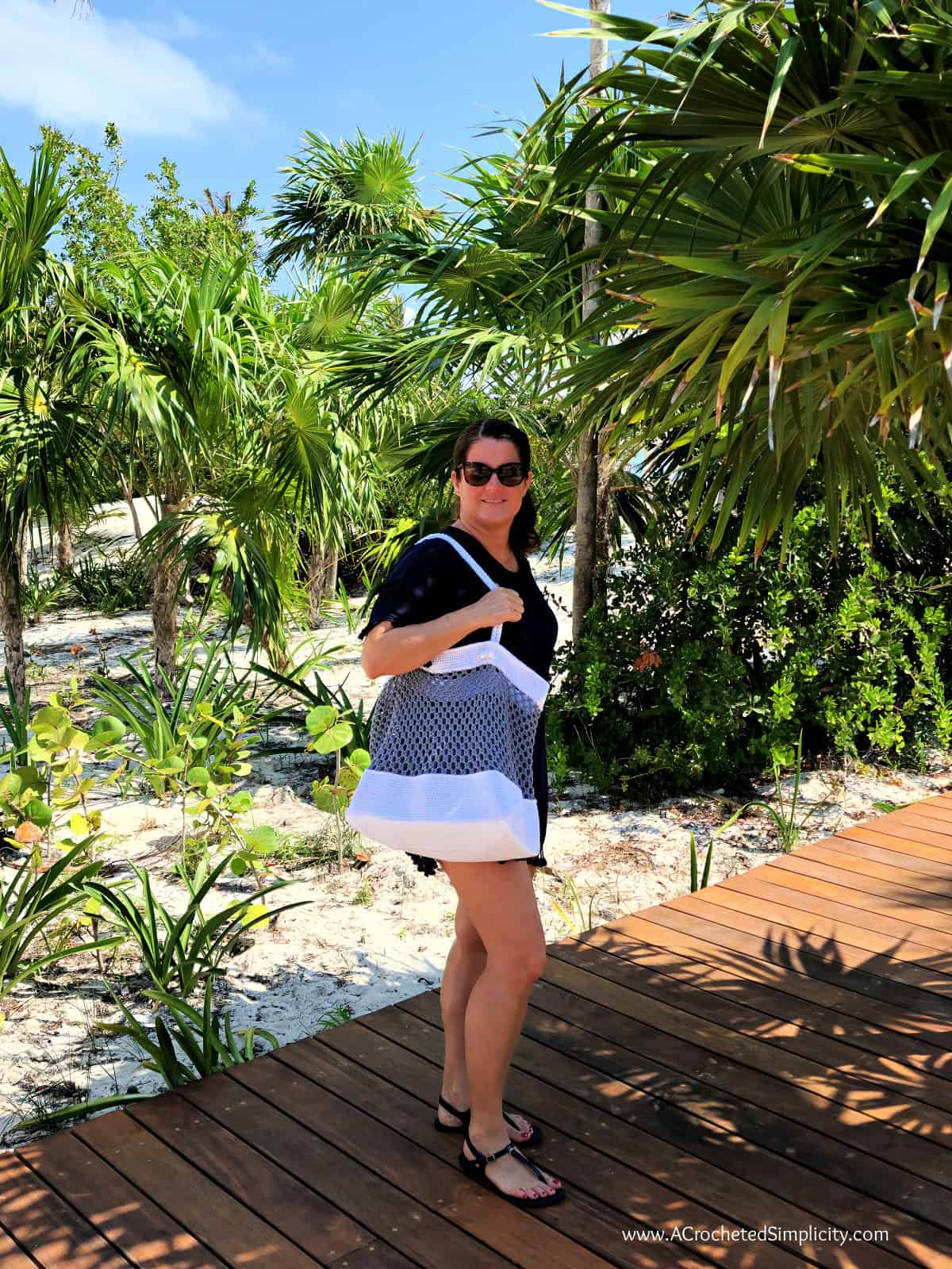 Woman by palm trees holding white and grey cotton crochet beach bag.