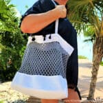 Woman carrying white and grey beach bag.