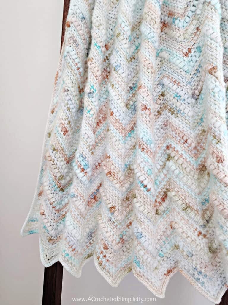 Crochet chevron blanket in beachy colors hanging on a blanket rack.