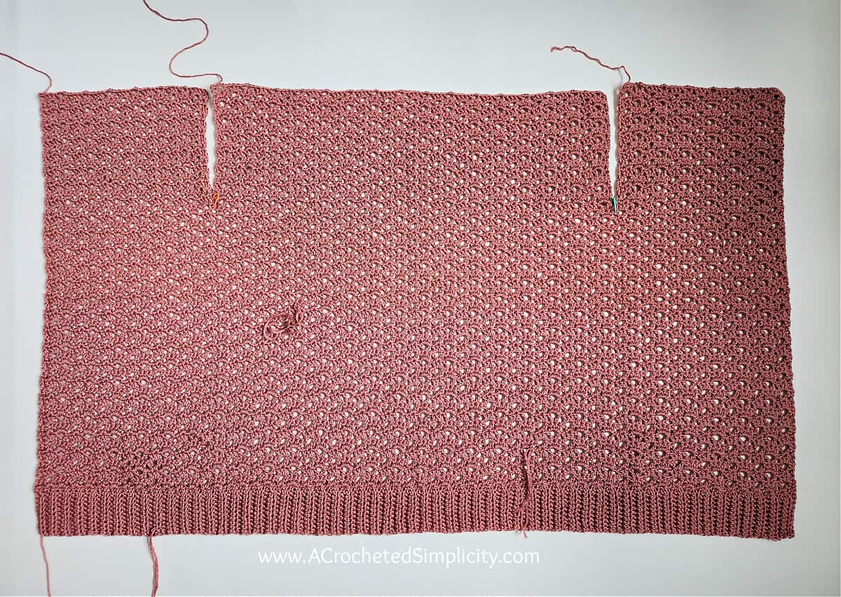 Crochet summer cardigan laid flat on a white surface before seaming the shoulders.