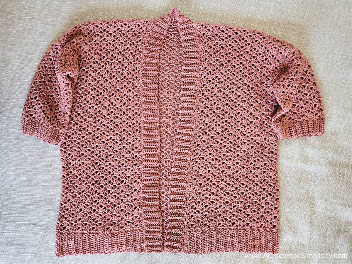 Mauve crochet summer cardigan laid flat on an ecru fabric showing the front ribbing completed.