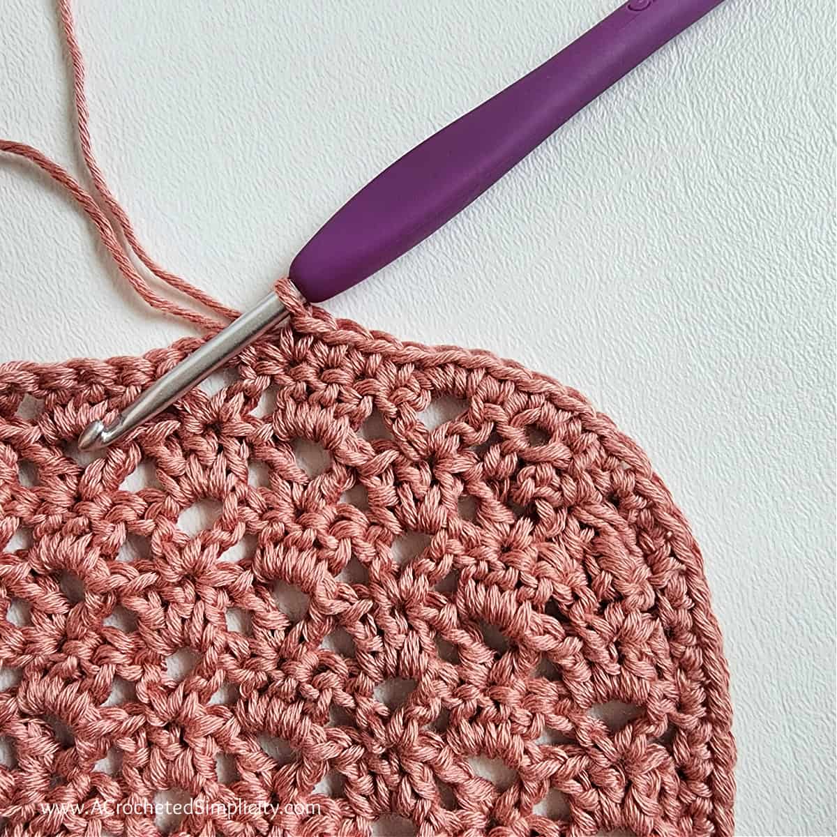 Close up of a purple crochet hook edging the cardigan pocket.
