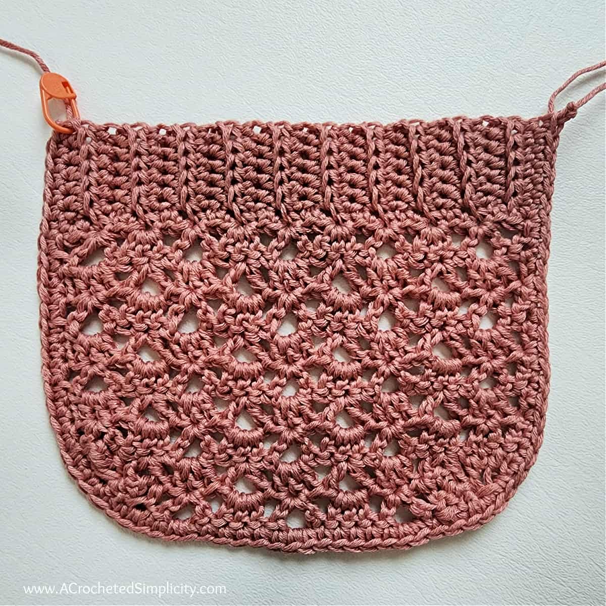 One mauve lacey crochet pocket laying on a white surface.