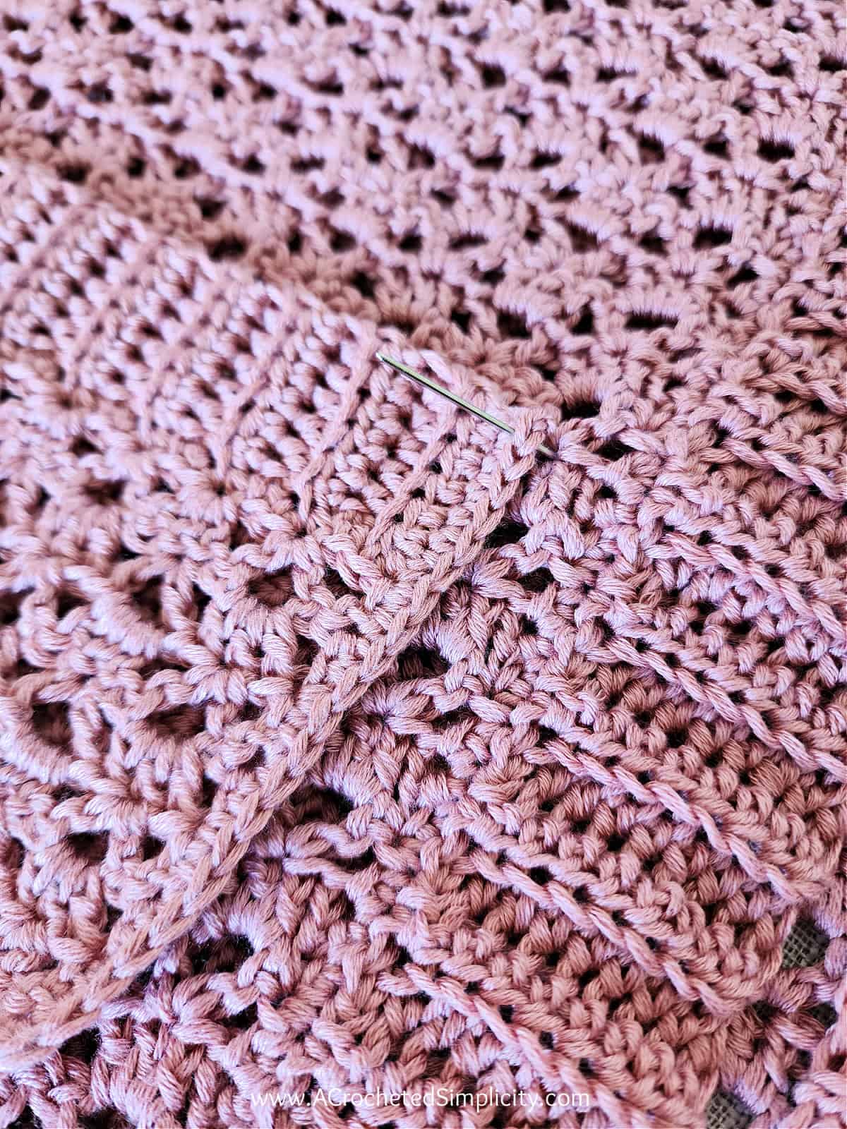 Close up of a yarn needle sewing the pocket onto the front of the cardigan.
