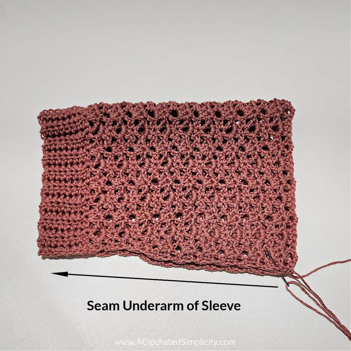 Tapered crochet sleeve with ribbed cuff folded in half to be seamed.
