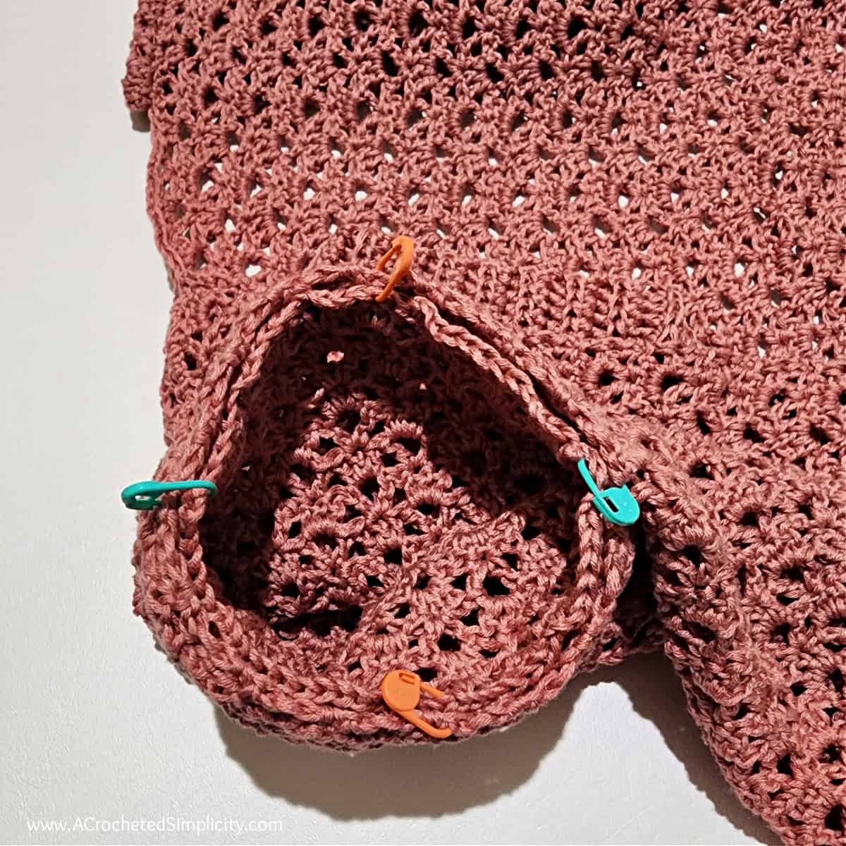 Four colored stitch markers holding the tapered sleeve in the armhole opening for seaming.