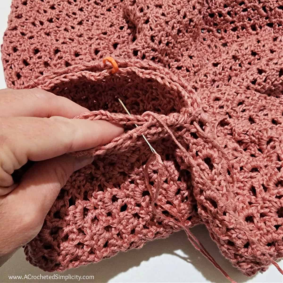 The sleeve is being attached to the armhole opening on the cardigan with a yarn needle and whipstitch.