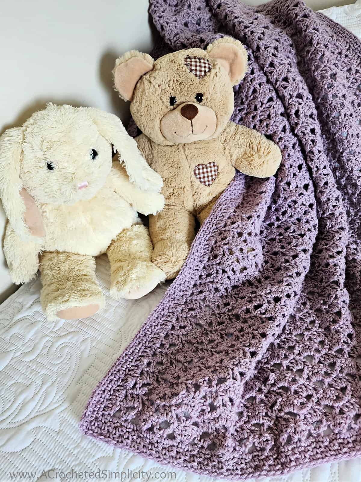 Lilac colored crochet lacy baby blanket with a cream colored stuffed bunny and light brown teddy bear