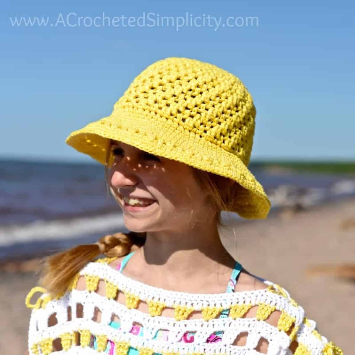 Young girl on the beach modeling a bright yellow crochet sunhat