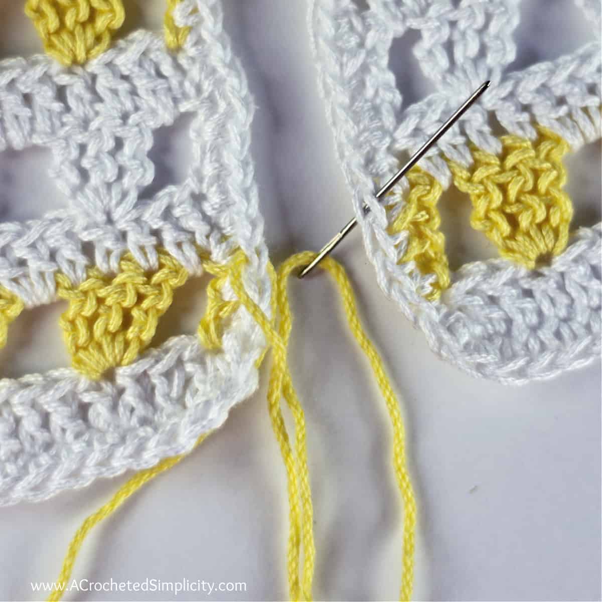 A needle with yellow yarn is inserted from bottom to top into the edge of the piece on the right.