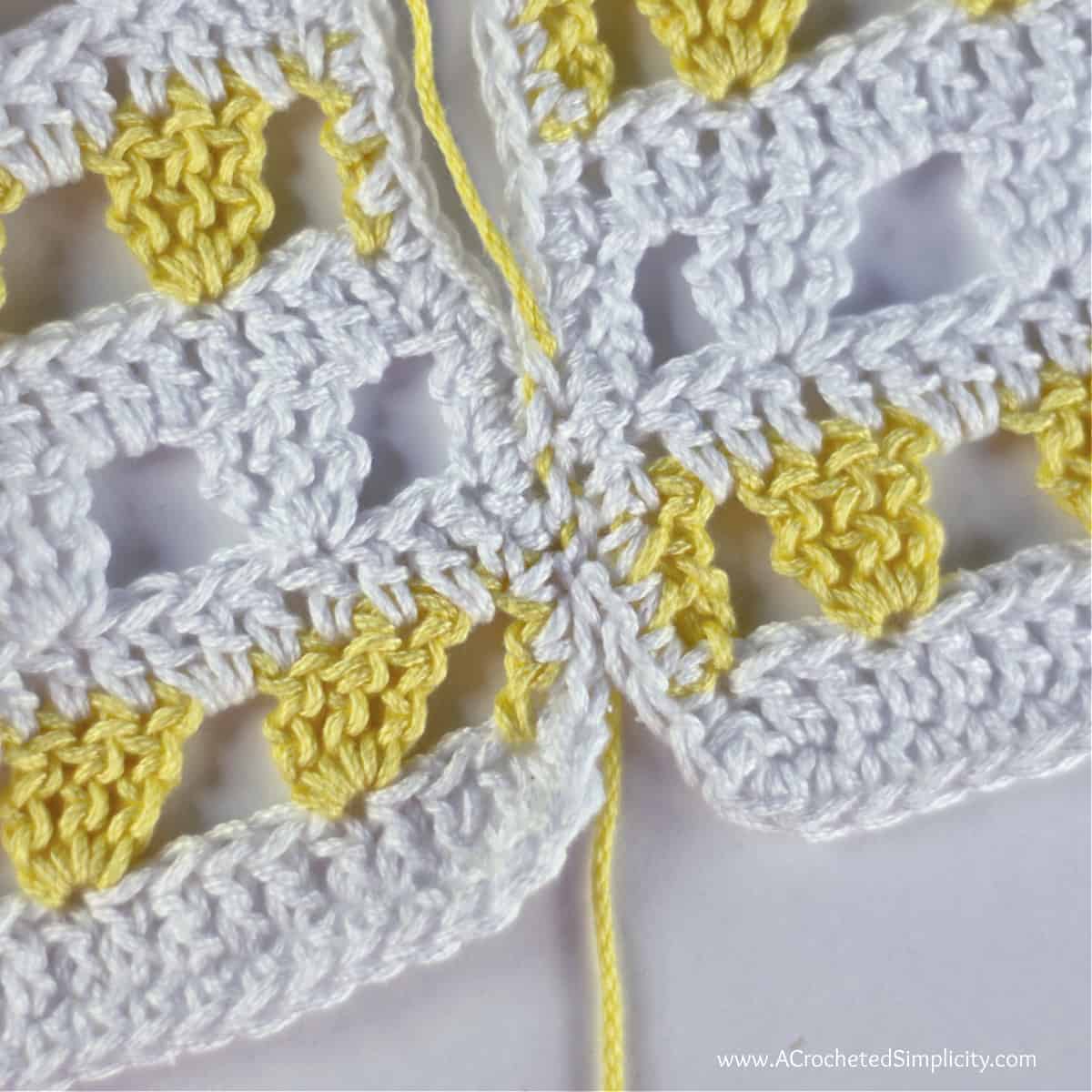 The yellow yarn is pulled on both ends to close the mattress stitch seam.