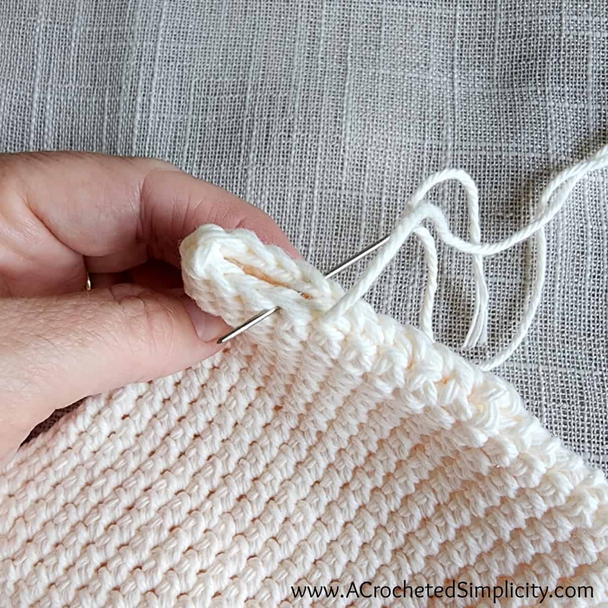 The bottom of a small crochet pouch being sewn shut with a whipstitch.