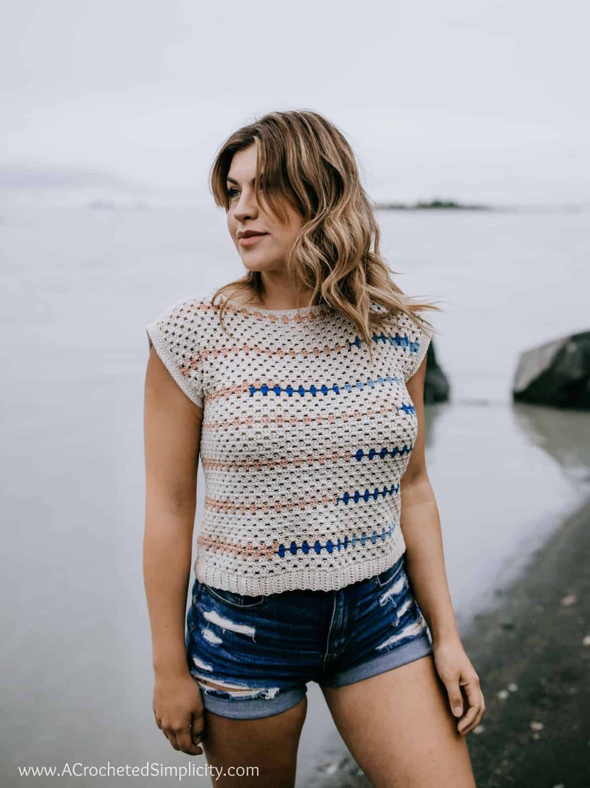 Cute crochet top being modeled by a woman near water.