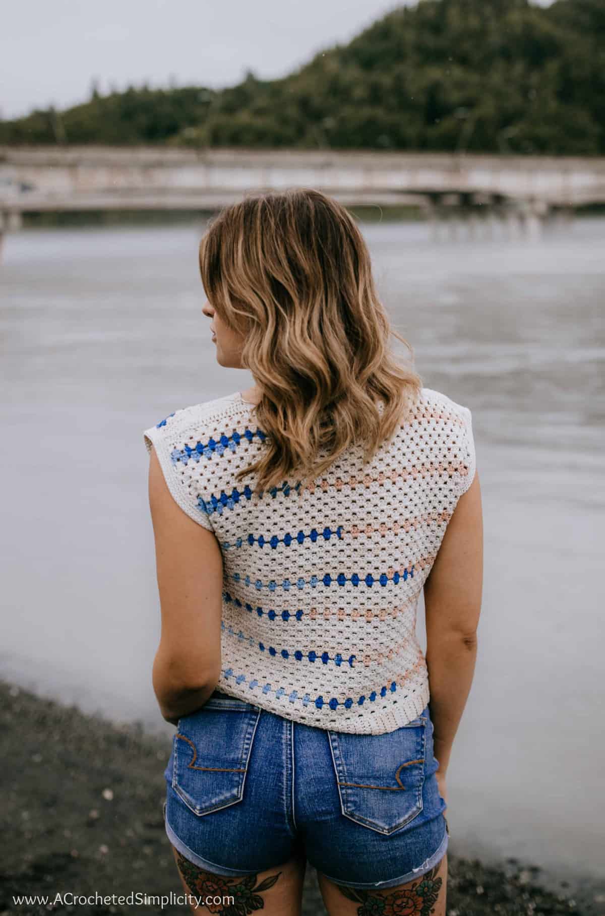 Backside of a model wearing a crochet granny stitch top in cream, pink and blue.
