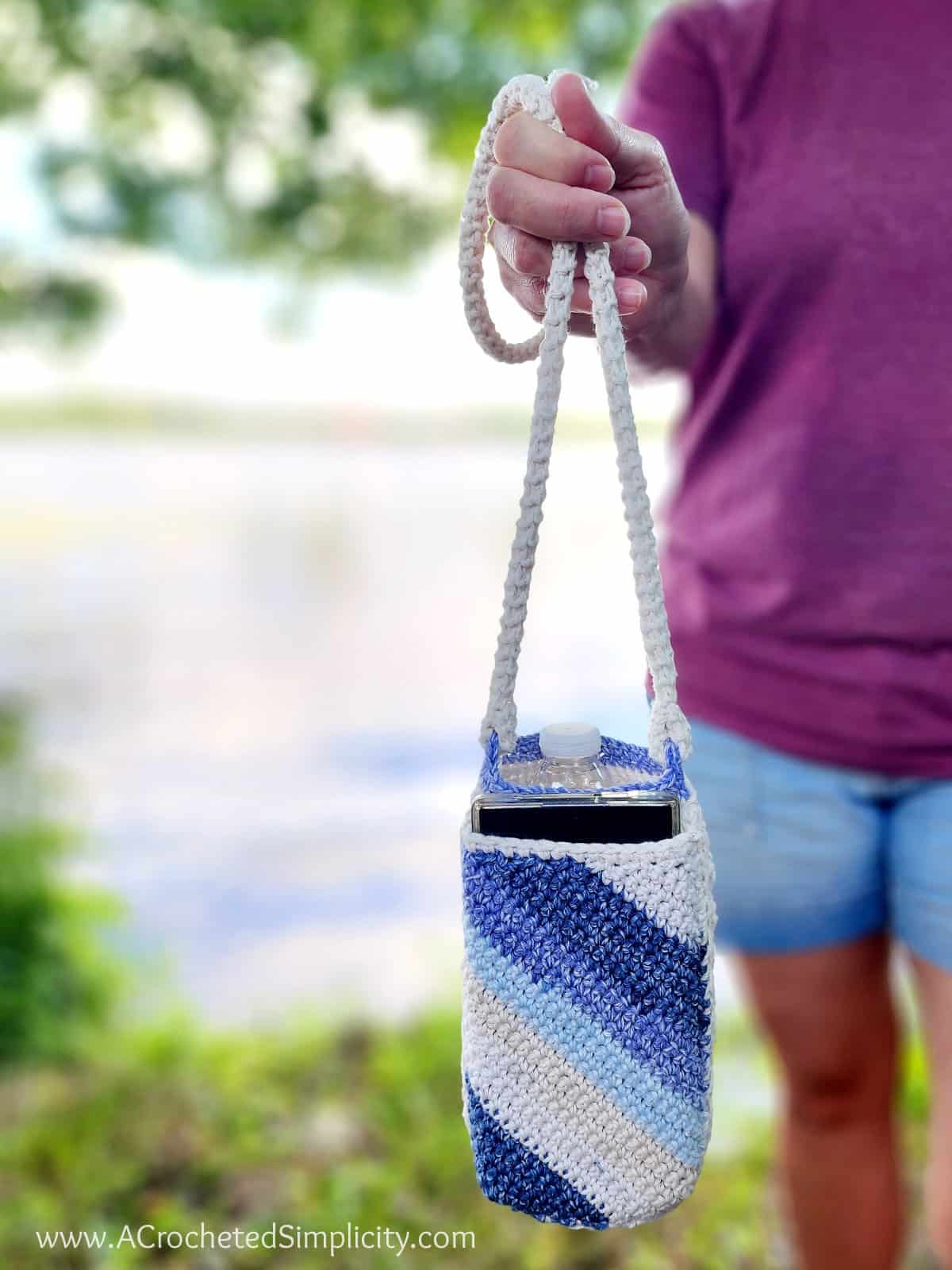 Close up of a cream crochet water bottle holder with a blue striped cell phone pocket.