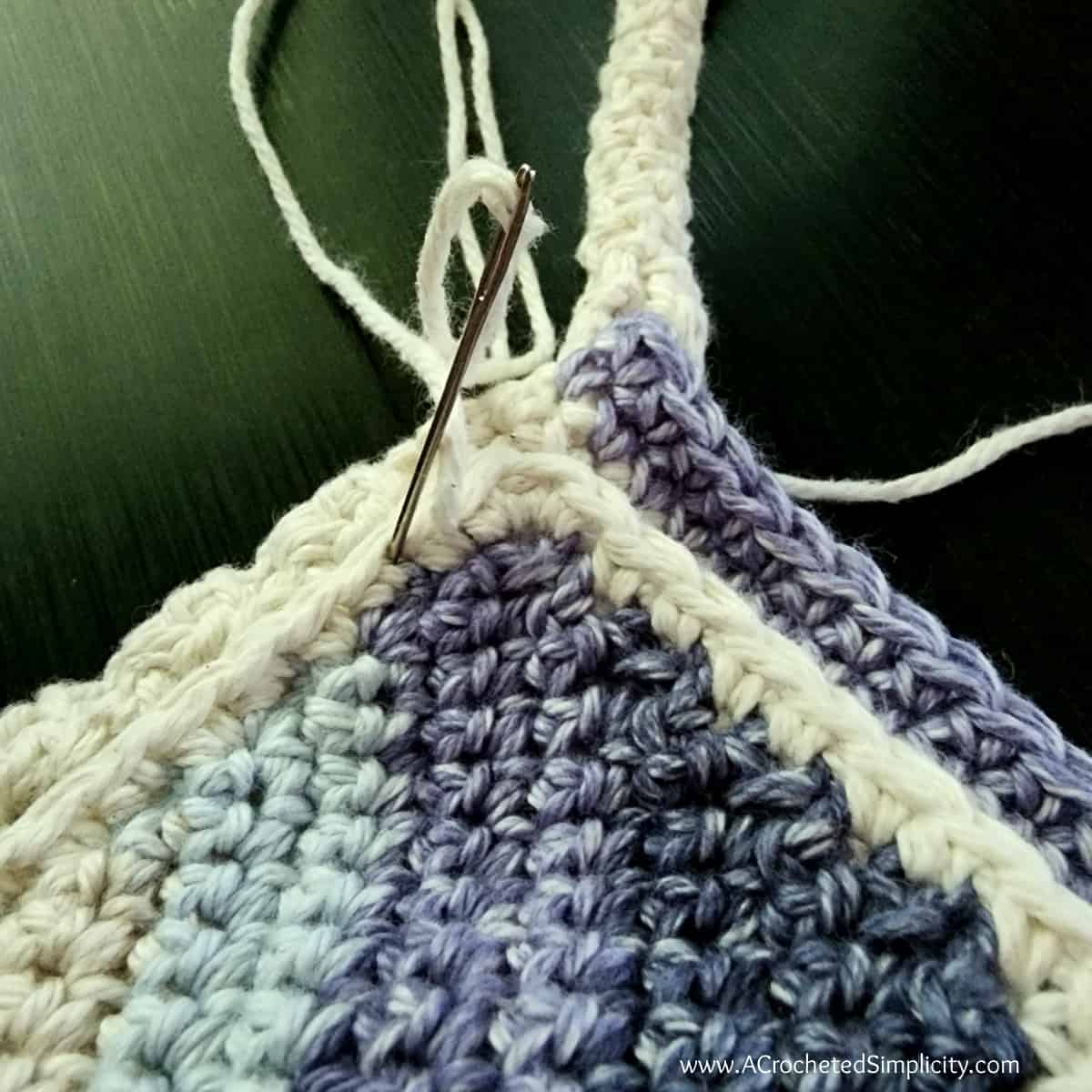 Crochet cell phone pocket being attached to the crochet water bottle holder with a yarn needle and whipstitch.
